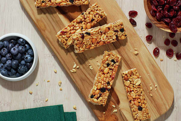 Five Nature Valley bars randomly arranged on a cutting board with bowls of blueberries and craisins"